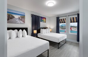 A hotel room with two beds, a painting of a beach scene, a view of a pool, and a window with curtains. - Snowbird 2BR Condo On The Boardwalk + 100 Dollar Resort credit (Myrtle Beach)