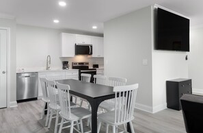 A modern kitchen with white cabinets, a black countertop, and a dining area with white chairs. - Snowbird 2BR Condo On The Boardwalk + 100 Dollar Resort credit (Myrtle Beach)