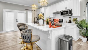Une cuisine moderne avec des meubles blancs, un four à micro-ondes en acier inoxydable et un îlot central doté de tabourets de bar.