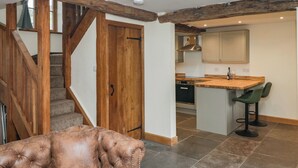 A spacious kitchen with wooden beams, a built-in island, and a dining area with green chairs. - Howgill Head (Kendal)