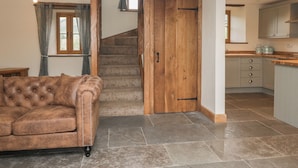 A cozy living room with a brown leather sofa, a wooden staircase, and a kitchen area with grey cabinets. - Howgill Head (Kendal)