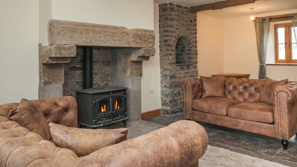 A cozy living room with a stone fireplace, a sofa, and a wooden ceiling beam. - Howgill Head (Kendal)