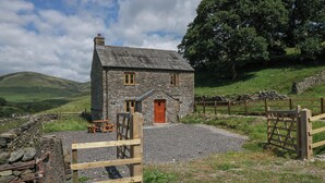 A stone house with a wooden door and windows, surrounded by a stone wall and a wooden gate. - Howgill Head (Kendal)
