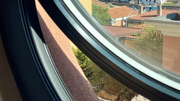 Uitzicht door een raam op een woongebied met huizen, een heldere lucht en een bergketen in de verte.