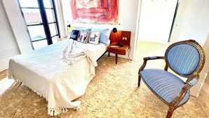 Een slaapkamer met een bed, een stoel en een groot abstract schilderij aan de muur.