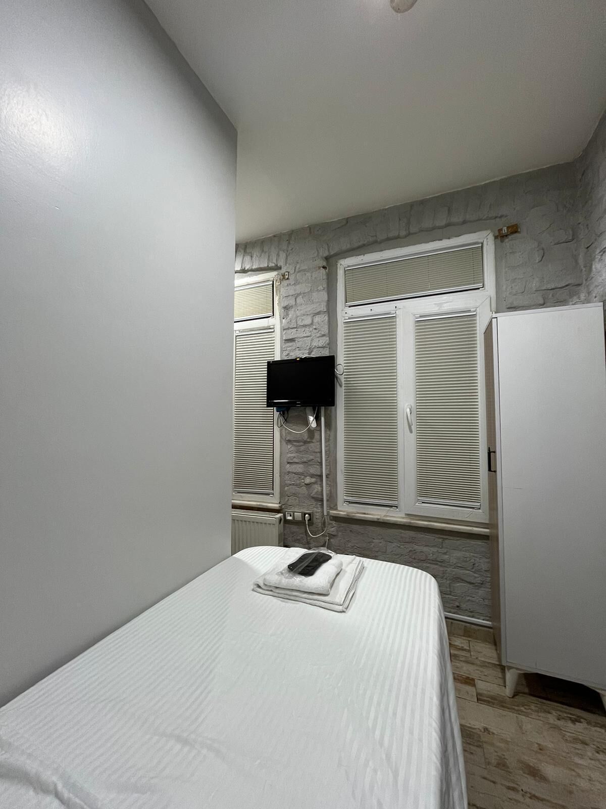 A bedroom with a bed, a white wardrobe, a radiator, and a window with shutters.