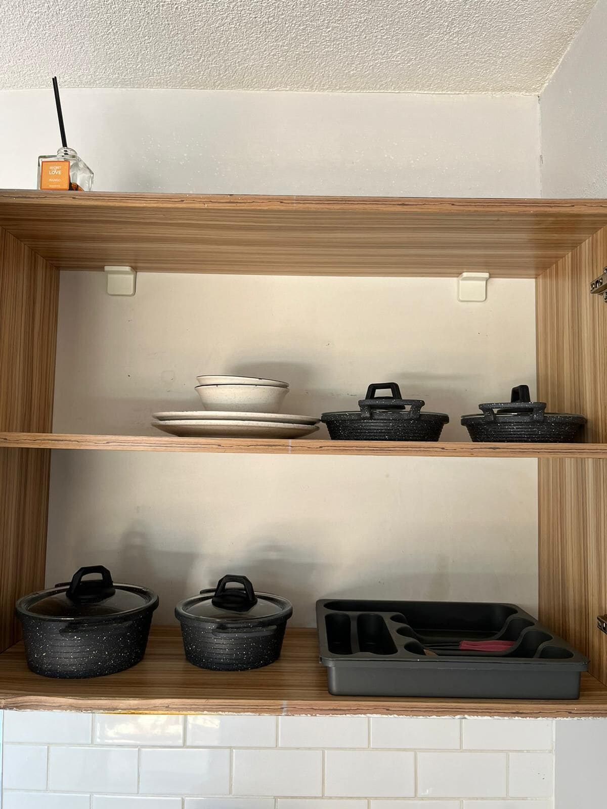 A kitchen with wooden shelves, a white tiled backsplash, and various kitchenware including pots, pans, and a baking tray.
