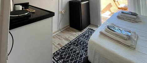 A compact hotel room with a bed, a small kitchenette, a TV, and a window with a view of buildings.