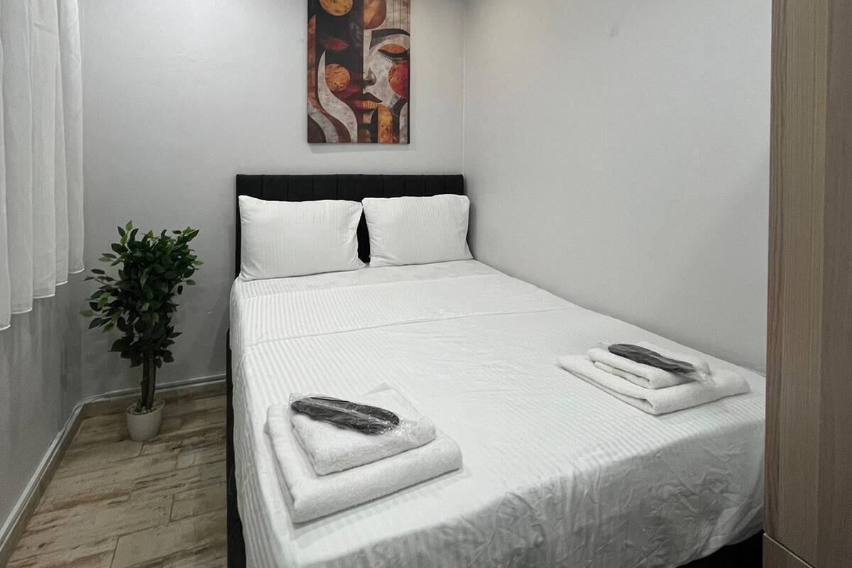 A modern hotel room with a neatly made bed, a potted plant, and a painting on the wall.