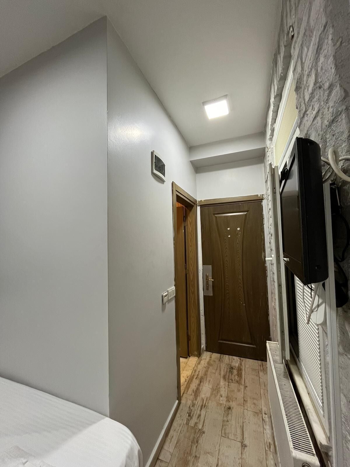 A narrow hallway with a wooden door, a white radiator, and a television mounted on the wall.