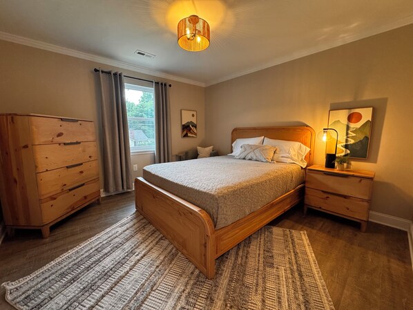 A bedroom with a wooden bed, a nightstand, a dresser, and a window with curtains.