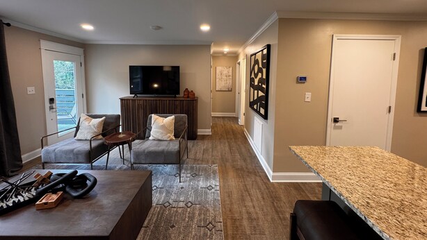 A modern living room with a flat-screen TV, a sofa, a coffee table, and a kitchen area with a granite countertop. - Quaint 2-bedroom apartment Historic downtown Florence (Florence)