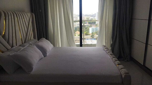 Ett modernt sovrum med en stor säng, en sänggavel med en unik design och utsikt över staden genom stora fönster.