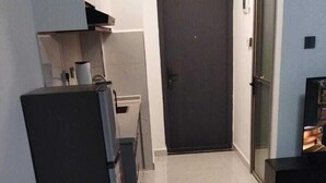 Ett kompakt bostadsutrymme med ett litet kök, en mörk dörr och en mönstrad matta.