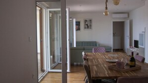 A modern living room with a wooden dining table, a sofa, and a glass door leading to a balcony. - Casa Bel Mare (Jelsa)