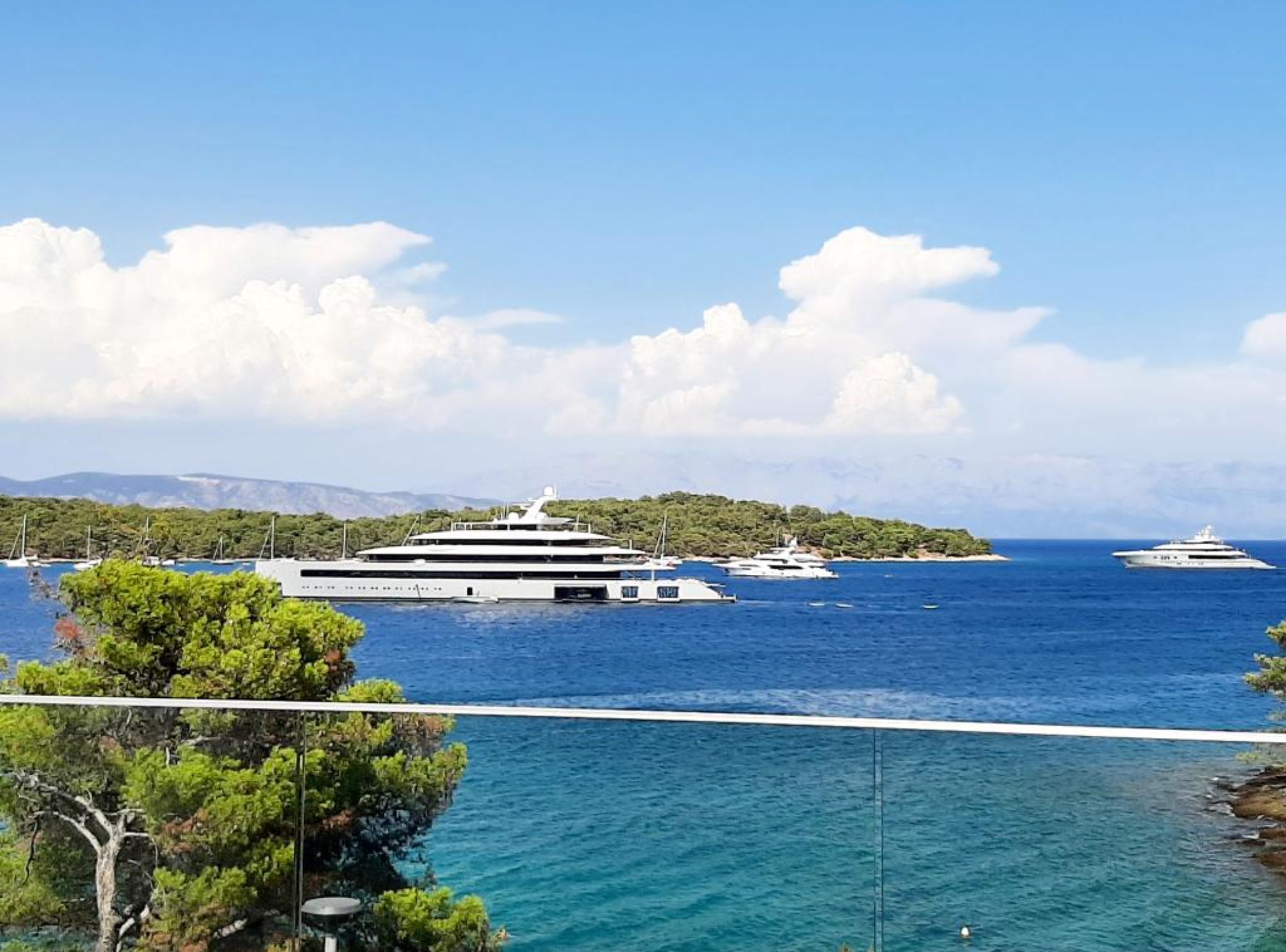 A large yacht docked at a marina with a clear view of the sea and distant mountains.