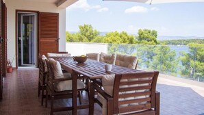 A wooden dining table with chairs on a balcony with a glass railing, overlooking a lake and trees. - Casa Bel Mare (Jelsa)