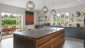 A modern kitchen with a large island, pendant lights, and a view of the garden through large windows. - Spacious Home, Hot Tub, Gym, Games Room & Garden (Hardington Mandeville)