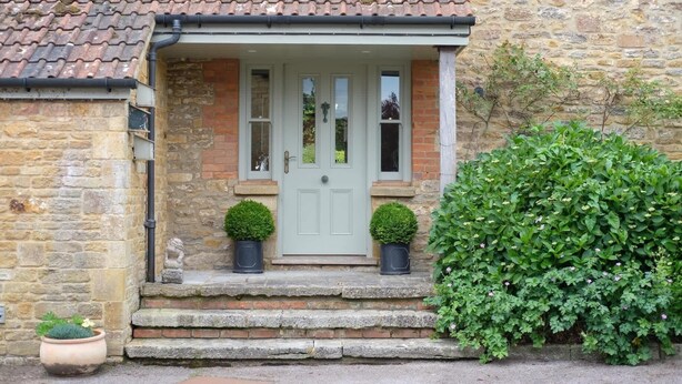 A stone house with a tiled roof, a front door, and a small porch with steps. - Spacious Home, Hot Tub, Gym, Games Room & Garden (Hardington Mandeville)