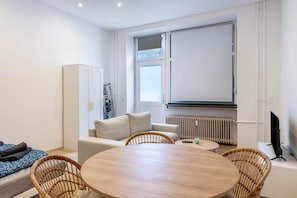 Une pièce moderne comprenant une table ronde en bois, des chaises en osier, un canapé, une armoire, un radiateur et un téléviseur.