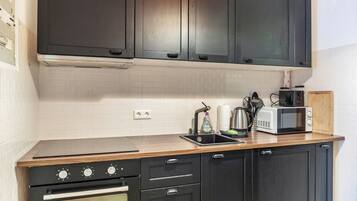 A kitchen with dark cabinets, a microwave, a kettle, and a wooden countertop.