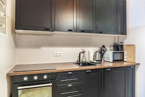 Une cuisine avec des meubles de rangement de couleur sombre, un four à micro-ondes, une bouilloire et un plan de travail en bois.