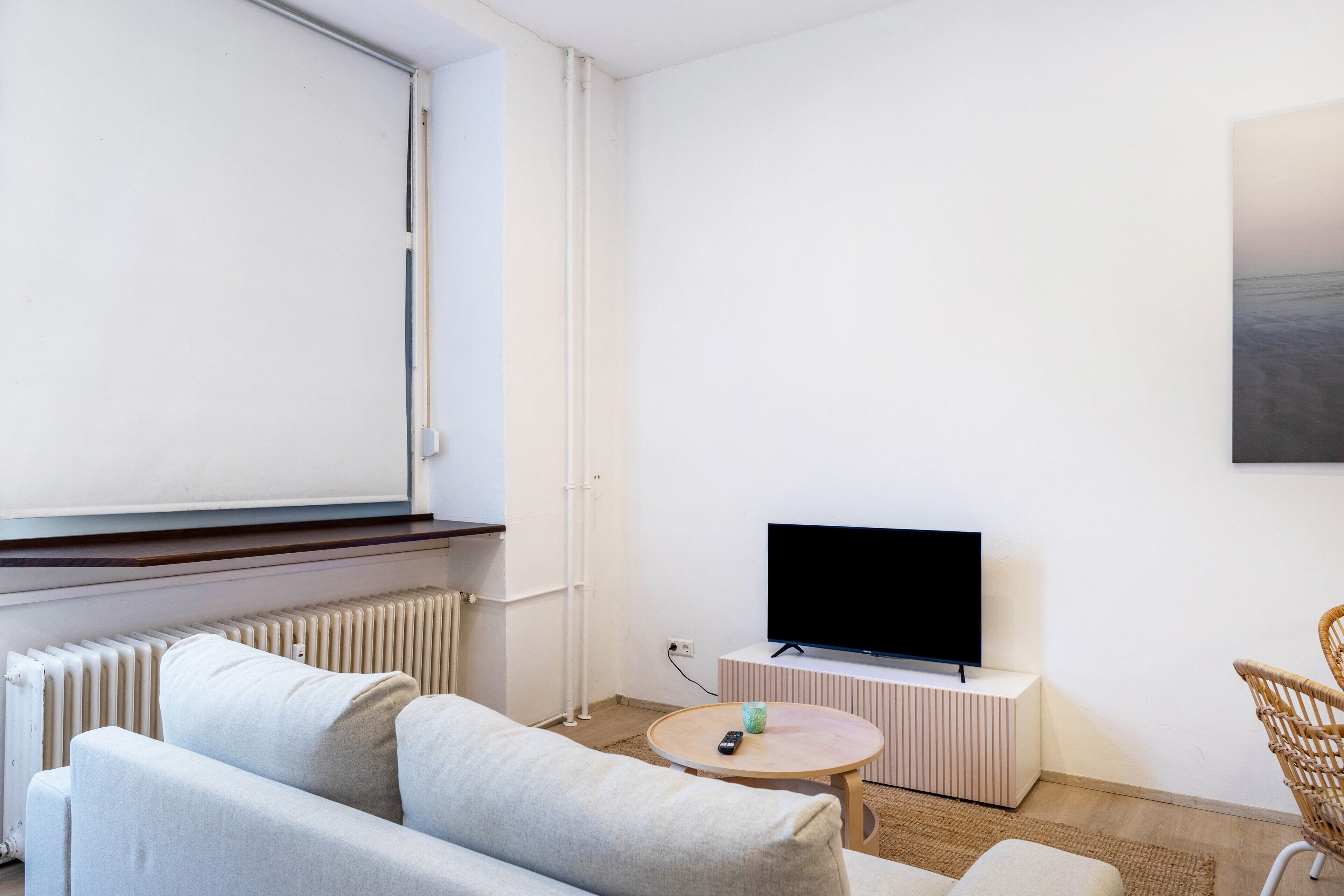 A modern living room with a sofa, a round table, a TV on a stand, and a radiator.