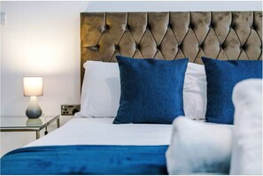 Ein ordentlich bezogenes Bett mit einer gebügelten Kopfteil, blauen und weißen Kissen sowie einer blauen Tagesdecke.