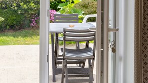 Puerta abierta que da a un patio con mesa y sillas, rodeado de follaje.