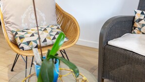 Sillas de mimbre con cojines, una planta en maceta y una mesa de cristal.