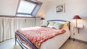 A bedroom with a skylight, a bed with a floral bedspread, two bedside lamps, and a wall-mounted shelf with a book. - Ty Annick – Les Glénans Room (Névez)
