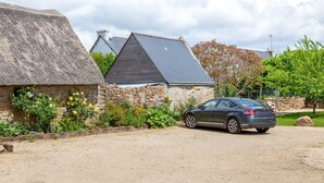 A stone building with a thatched roof, a parked car, and a gravel driveway. - Ty Annick – Port Manech Room (Névez)