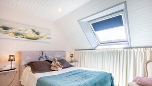A bedroom with a sloped ceiling, a skylight, a bed with a blue blanket, a chair, and a teddy bear. - Ty Annick – Port Manech Room (Névez)