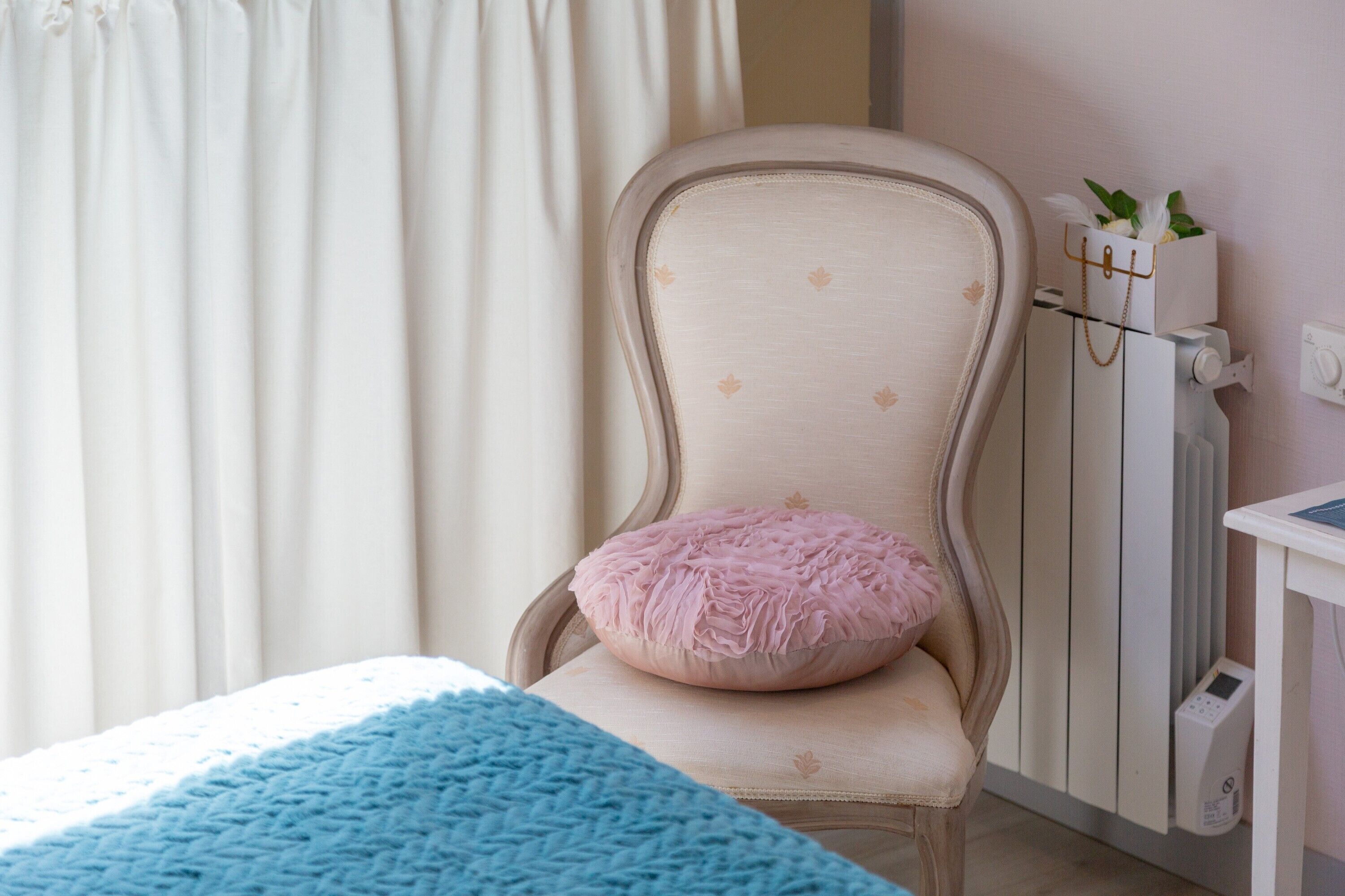 Une pièce comprenant un lit, une chaise avec un coussin, un radiateur et une petite table sur laquelle est posée une plante.