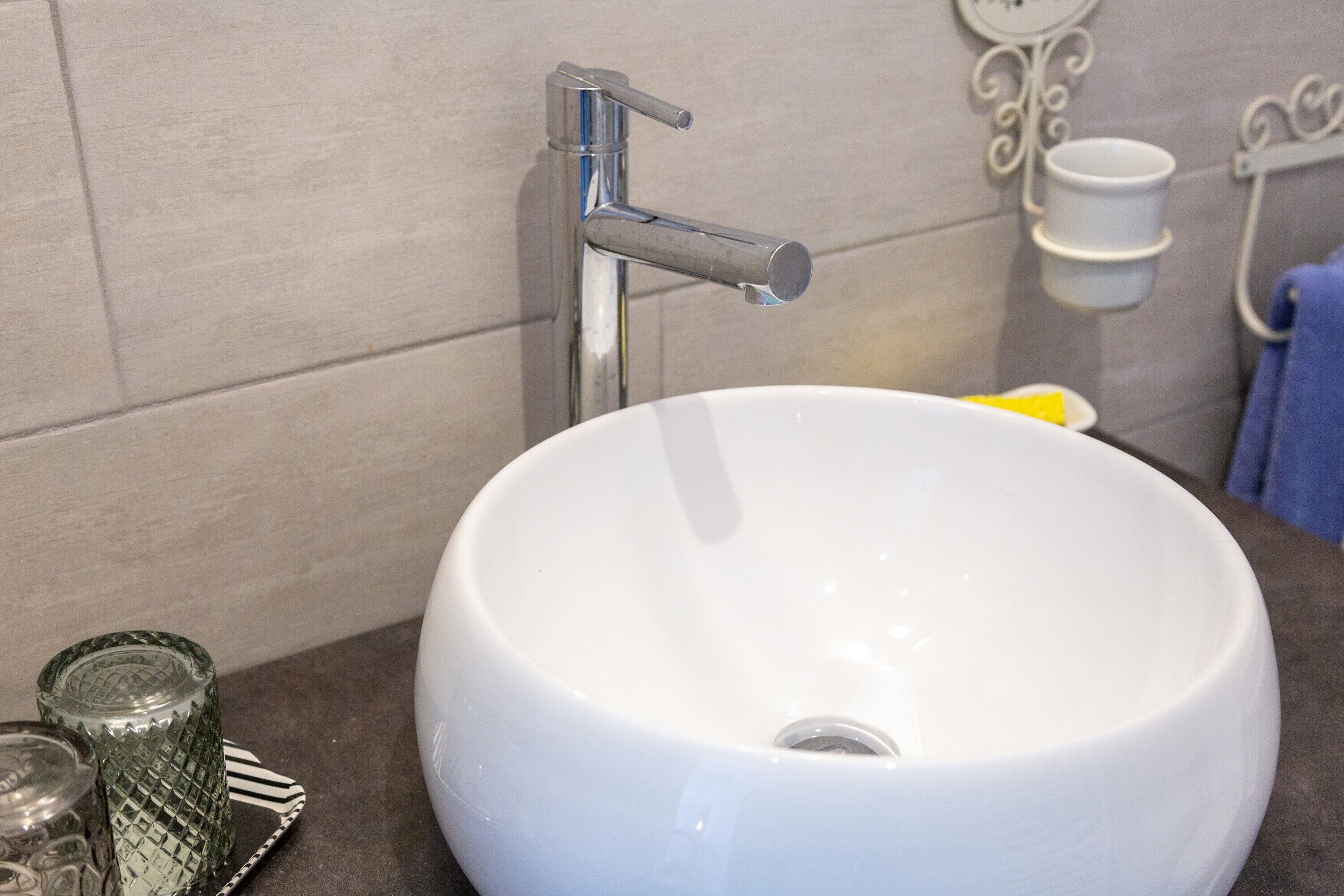A bathroom with a white sink, a chrome faucet, a glass container, and a white cup holder on the wall.