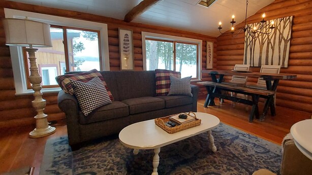 A cozy log cabin interior with a sofa, a dining table, and a patterned rug. - Ely Lakeside Cabin: The Perfect Northwoods Retreat (Ely)
