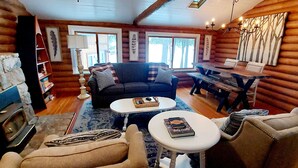 A log cabin interior with a fireplace, sofa, coffee table, and dining table. - Ely Lakeside Cabin: The Perfect Northwoods Retreat (Ely)