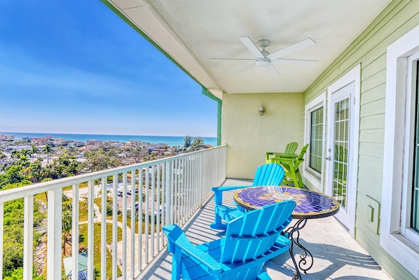 Un balcon avec vue sur l’océan, un ventilateur de plafond, ainsi que des chaises et une table bleues.