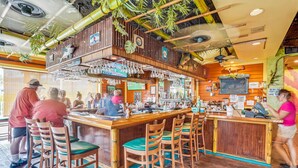 A bar area with wooden bar stools, a counter with a cash register, and various bar tools. - Harbourside 8816 (Indian Rocks Beach)