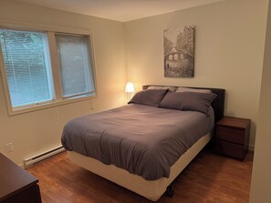 A bedroom with a bed, bedside tables, a lamp, a window with blinds, and a wall-mounted artwork. - Lakefront house with private dock (Lake Cowichan)