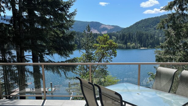 A balcony with a glass table and chairs overlooking a lake and forested hills. - Lakefront house with private dock (Lake Cowichan)