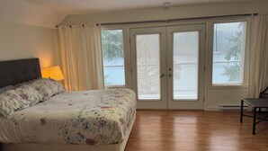 A bedroom with a bed, a nightstand, a lamp, a desk, and a sliding glass door with blinds. - Lakefront house with private dock (Lake Cowichan)
