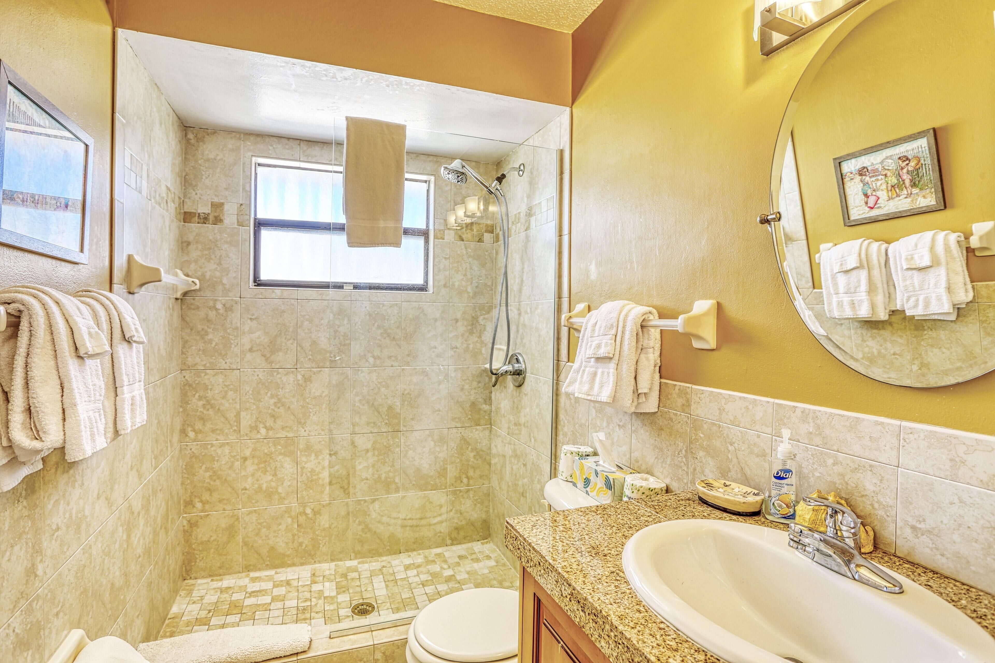 A bathroom with a shower, toilet, sink, and a window.