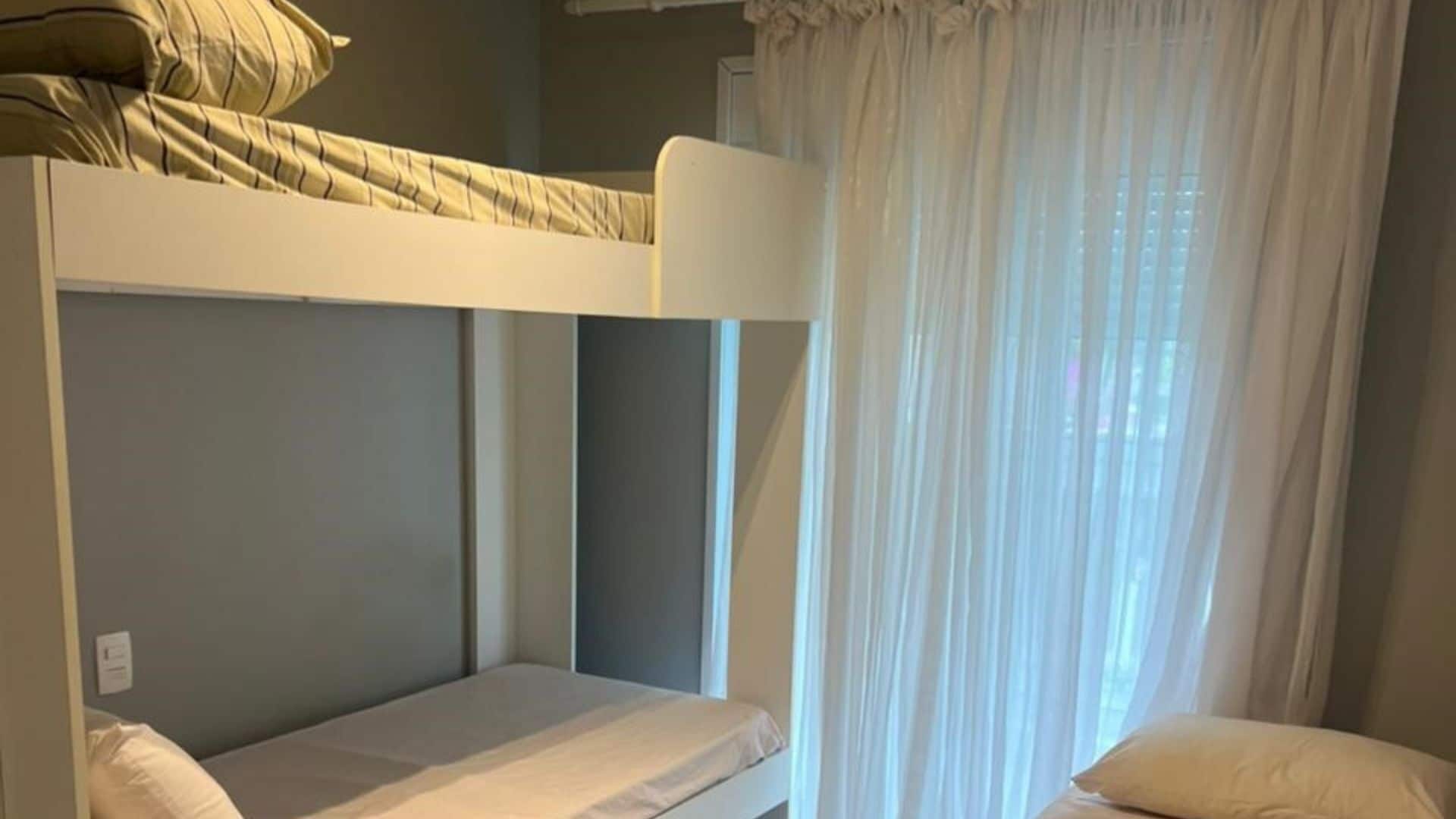 Quarto com beliche, janela e cortinas.