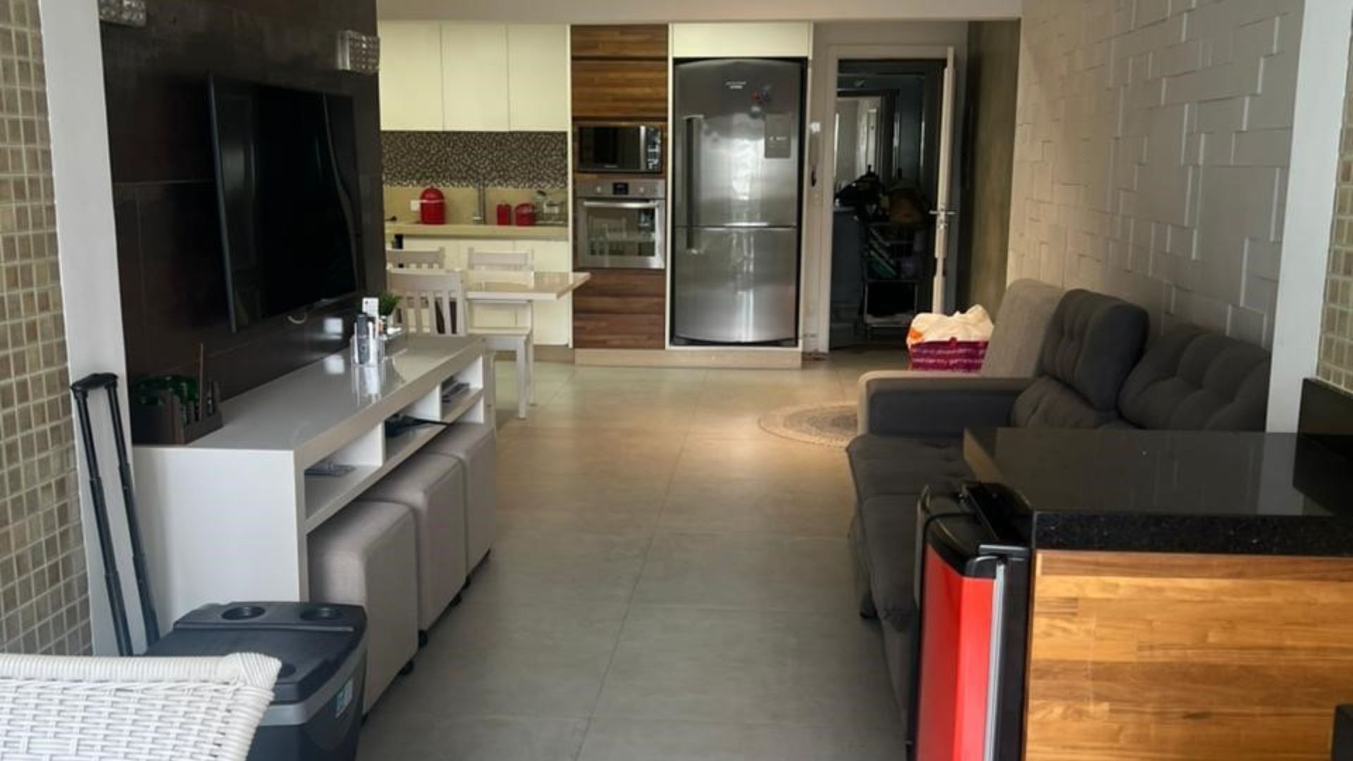 Cozinha moderna com forno embutido, micro-ondas e frigorífico. Há uma área de refeições com mesa e cadeiras brancas. Um sofá cinzento está na sala de estar.
