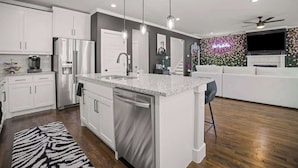 Une cuisine moderne avec des meubles blancs, des appareils en acier inoxydable, un îlot central doté d’un comptoir en granit et un tapis à motifs noir et blanc.