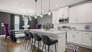 Une cuisine moderne avec des meubles blancs, un îlot en granit et des tabourets de bar noirs.
