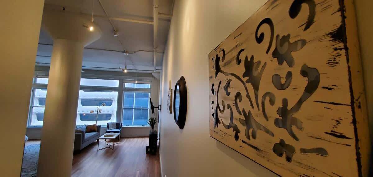A hallway with a large abstract painting, a round mirror, and a view of a parked van through a window.