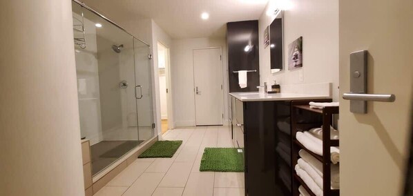 A modern bathroom with a glass shower enclosure, a sink with a mirror, and a towel rack. - Studio Loft with King Bed Downtown (Dallas)