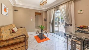 A spacious living room with a sofa, a small table with a plant, and a glass table with a fruit bowl. - Family Suite - Indoor Hot Tub, Heated Pool, Play Park & Table Mountain Views (Cape Town)